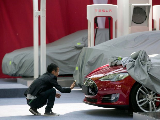 A man takes a photo of the logo on a Tesla Model S sedan at an event in Beijing, China, Tuesday, April 22, 2014. Tesla Motors delivered its first eight electric sedans to customers in China on Tuesday and CEO Elon Musk said the company will build a nationwide network of charging stations and service centers as fast as it can.Ng Han Guan/AP