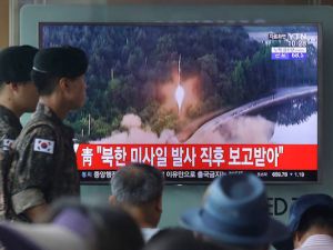 Army soldiers walk by a TV news program showing a file image of a missile being test-launched by North Korea in Seoul on Tuesday.